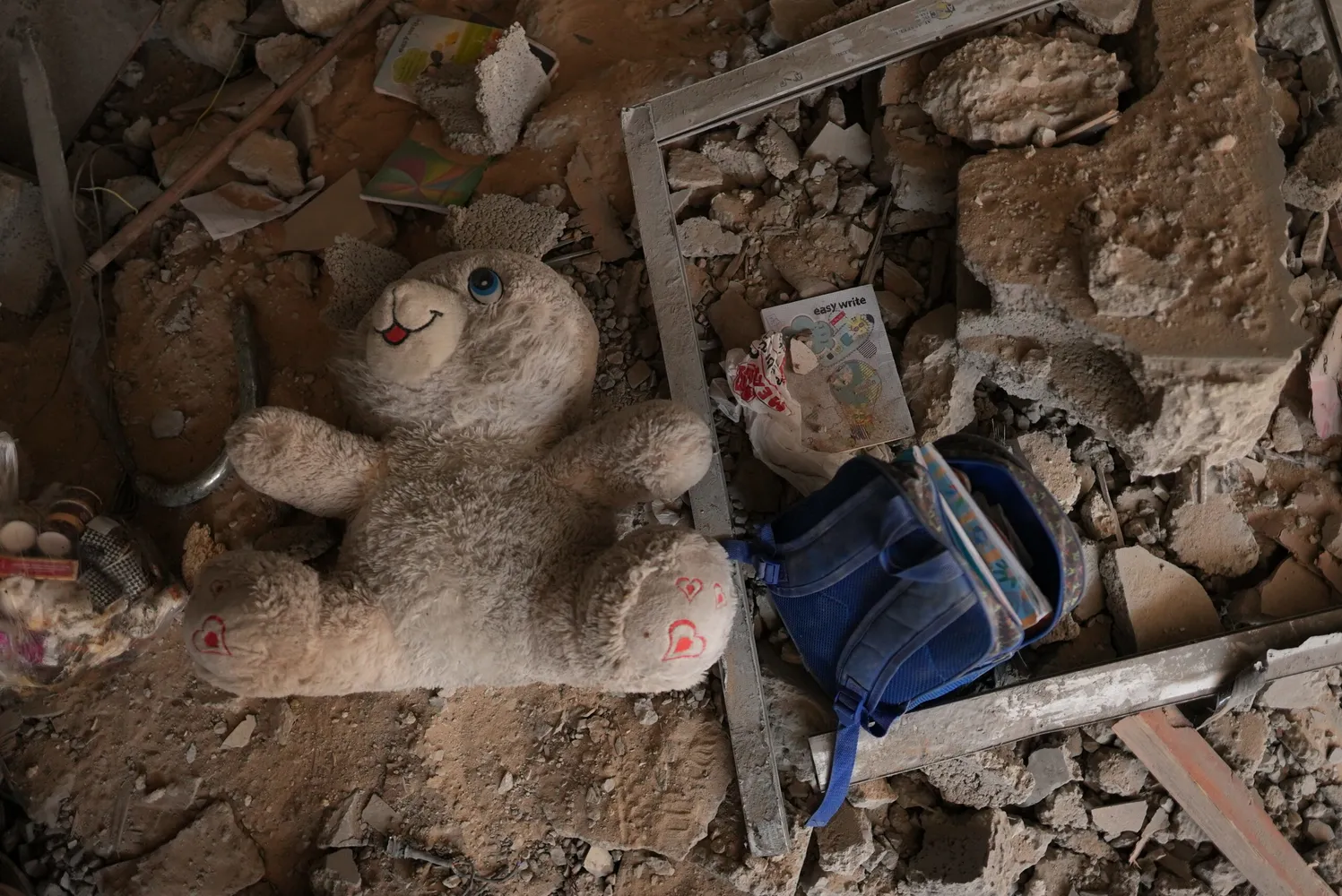 A child school backpack and a doll among a rubble in Gaza scaled.